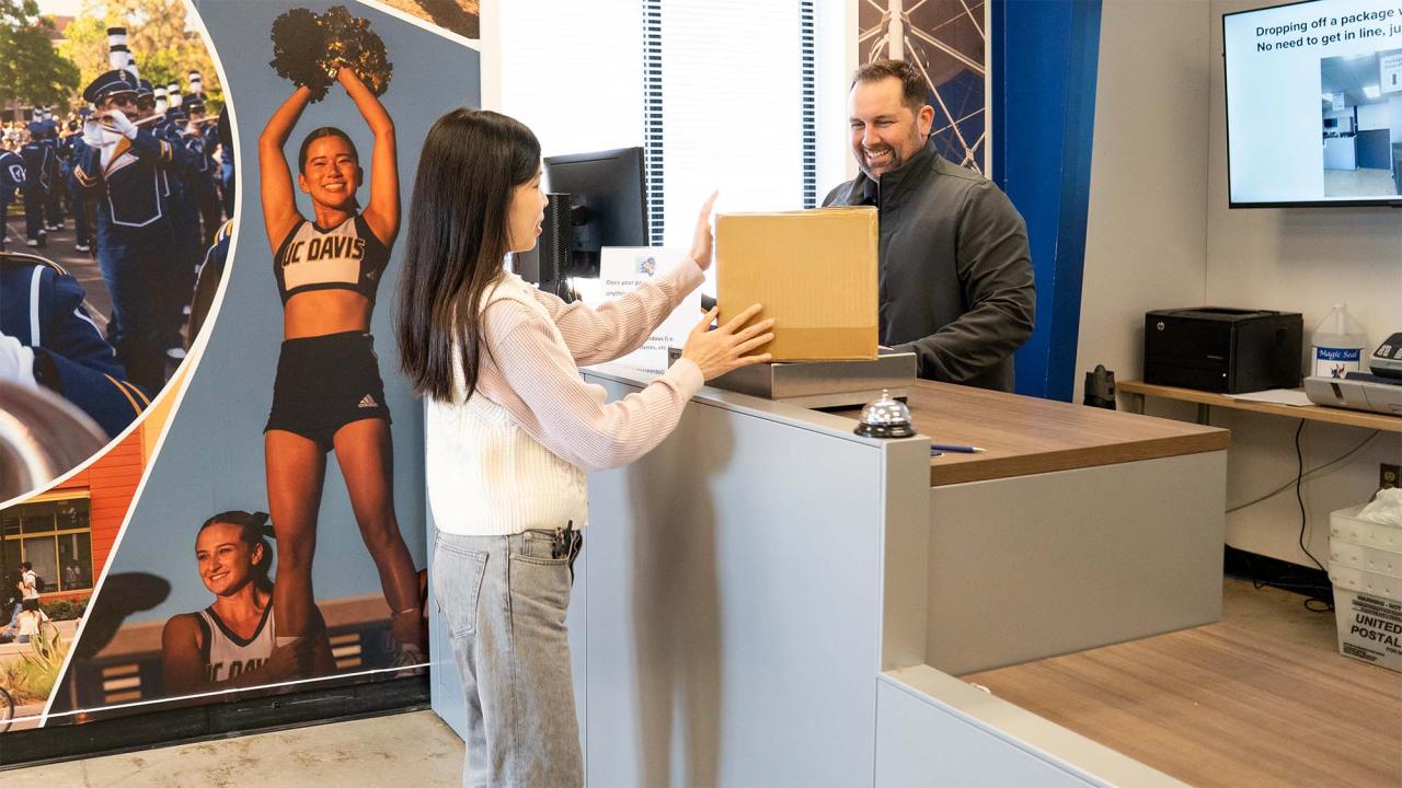 A woman hands a package to a smiling man at a service counter in a modern office setting.