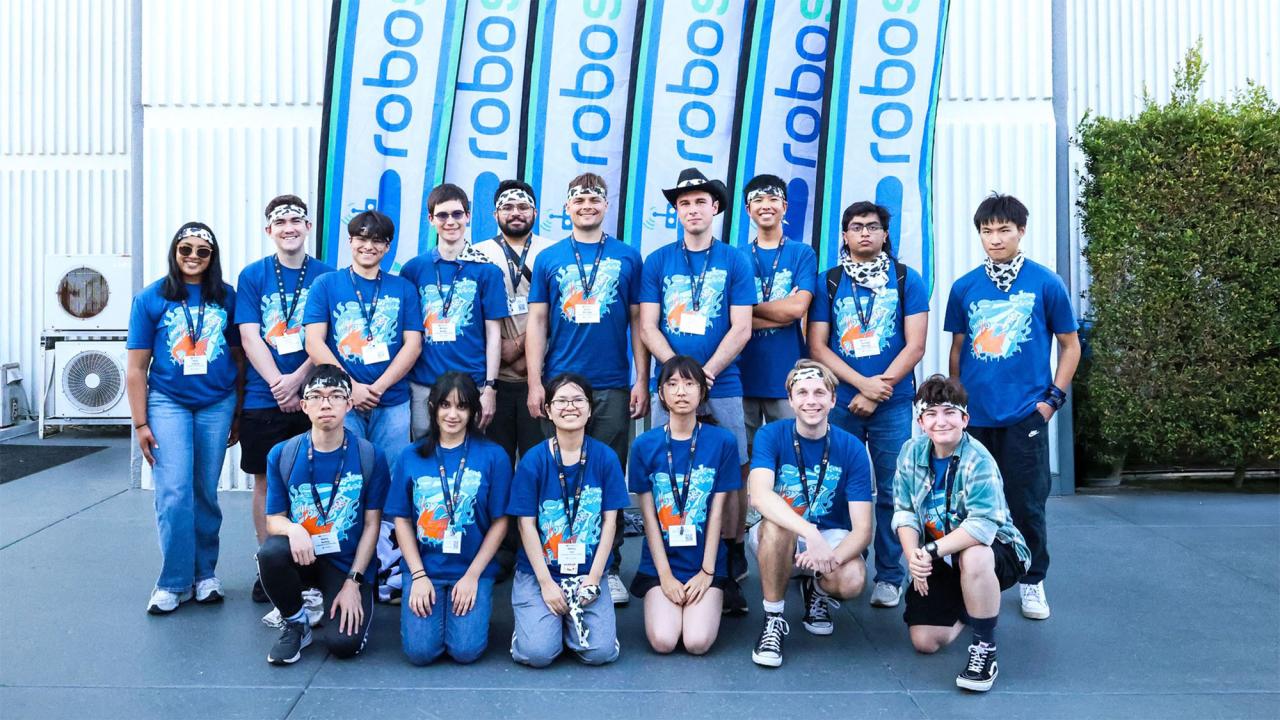 Group of people wearing blue matching T-shirts poses in front of flags that read "RoboSub"