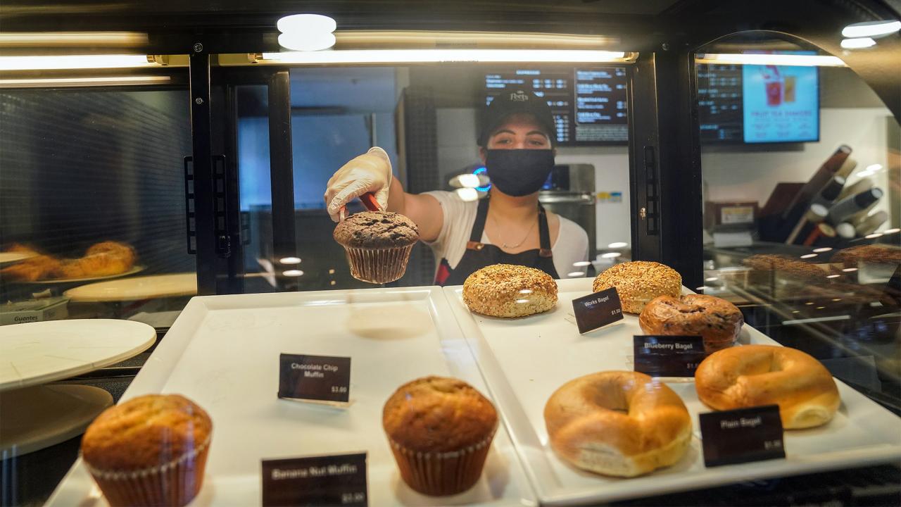 Woman takes pastry out of case.