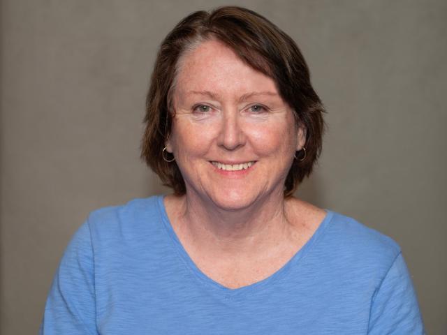 Smiling woman with short brown hair, wearing a blue sweater, in a library setting.