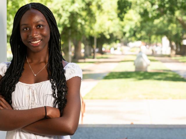 Student stands with her arms crossed with campus in the background