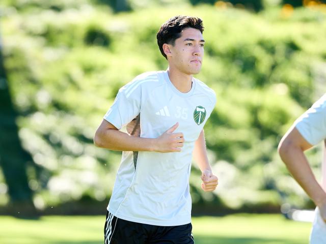 A young athlete jogging on a bright green field, wearing a white jersey and black shorts.