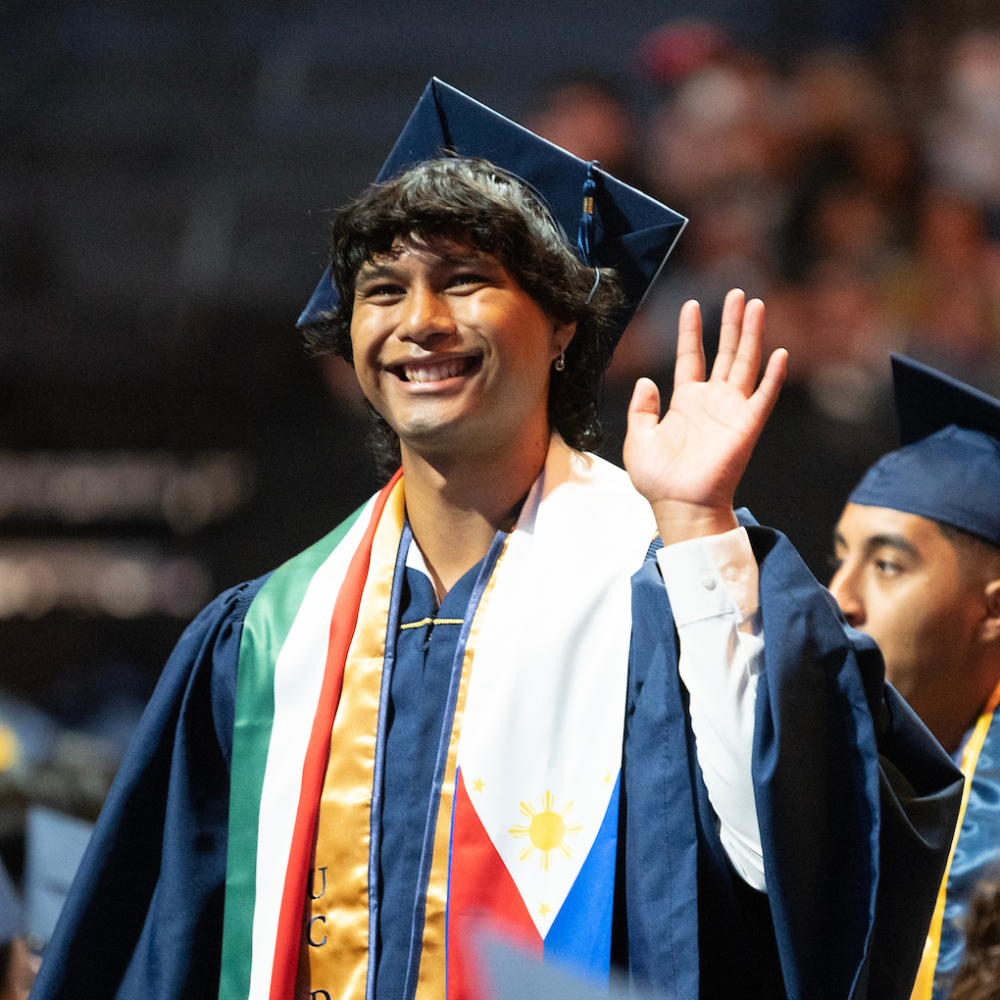 Smiling graduate in cap and gown waves.