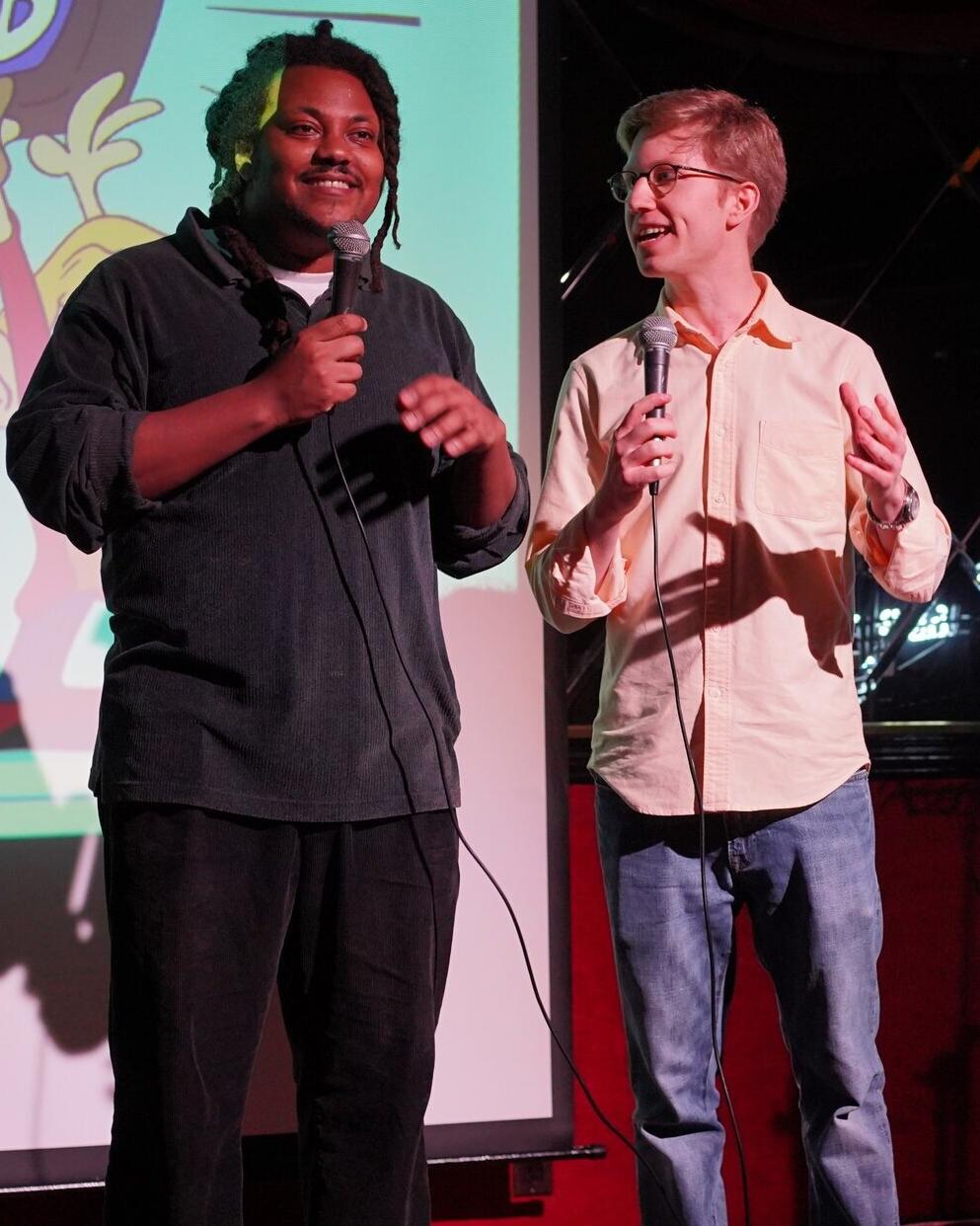 Two people stand on a stage holding microphones