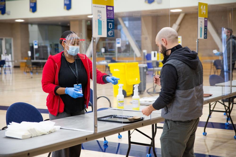 A woman shows a man how to properly do a COVID spit test.