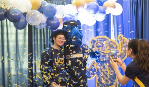 An incoming Aggie celebrating with Gunrock while another student takes their picture. 