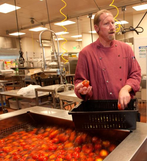 Chef stands next to vat of tomatoes, being cooked