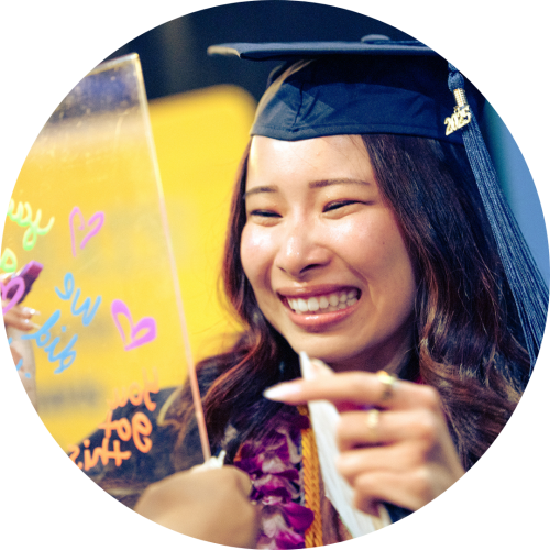 Smiling female graduate in cap and lei writing on a clear acrylic board