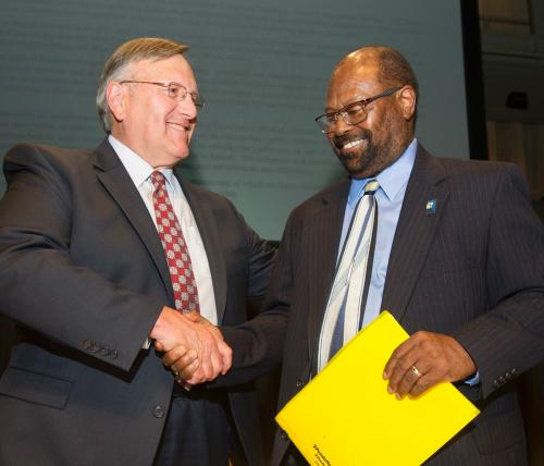 Two men, smiling, shake hands.