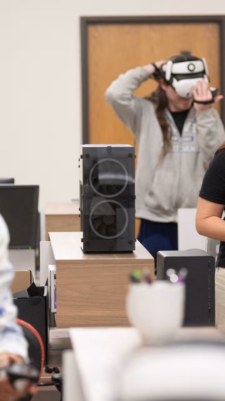 Classroom scene with two people wearing VR headsets at desks, instructor in foreground.
