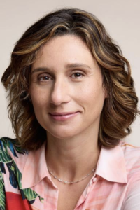Smiling woman with wavy highlighted hair and pink floral blouse, portrait photo