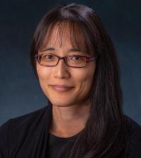 A headshot of a woman against a dark blue background, smiling.