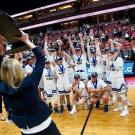 Basketball players cheer as coach holds Big West Conference trophy.