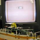 This robot was designed with the same basic senses and motor skills as a rat pup. The television screen shows a videotape of  the robotic rat moving about inside its rectangular arena.