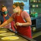 Two women cook burritos.