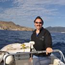 Man on boat in water with bare hills behind