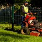 Man wearing mask stands on lawn mower.