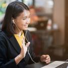 Woman, with earbuds, waves to computer screen, during a virtual interview.