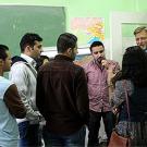 A group of men and one woman talking to a man in a beard in a classroom