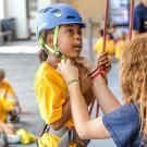 Camp leader puts helmet on girl at rock climbing wall.