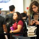 Alyxx Melendez checks prices on books while waiting in line