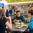 Three students, sitting around a table at a UC Davis dining commons, facing each other, eating and talking. 