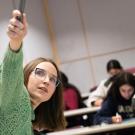 A woman professor points up to the board while students look on