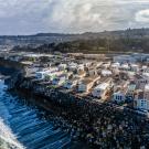 Aerial photo of coastal homes on rocky shoreline with crashing waves and cloudy sky