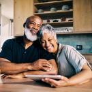 Two dark complected people sitting next to coffee cup in kitchen