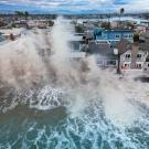 Aerial photo of massive waves crashing into beachfront homes, water flooding streets