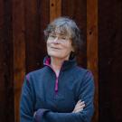 A woman stands in front of a wooden fence.