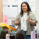 Teacher gestures while speaking to elementary students in a colorful classroom