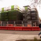 Two students walk past a construction site with scaffolding and safety barriers.