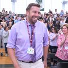 Smiling man in purple shirt walks past applauding crowd in gymnasium