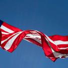 An American flag waves in the wind against a blue sky.