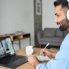 A man wearing headphones listens to someone on a computer screen