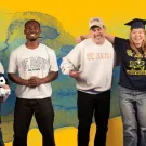 Smiling diverse group of six in a photo, one wearing a graduation cap, against a colorful backdrop