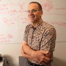 Man stands next to whiteboard, which is covered with writing