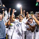 soccer players and coahces cheer and hold a trophy