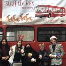 Five people stand against the side of a Unitrans double-decker bus