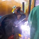 Three students in welding helmets bring bright white flame to their projects.