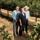 3 people stand in a vineyard