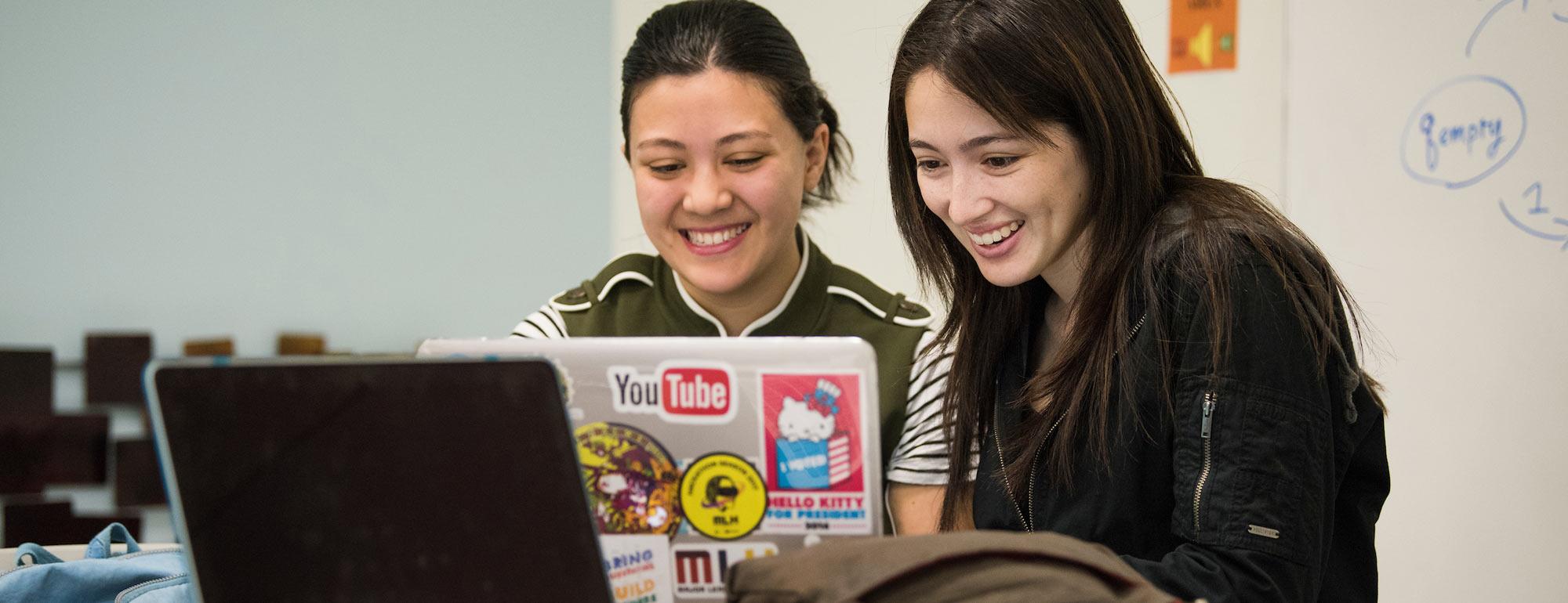 Two female students share a laptop to evaluate their work.