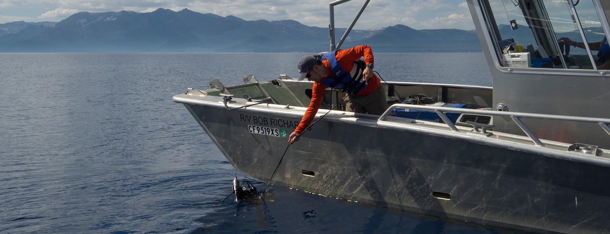 A researcher reaches into the waters of Lake Tahoe to secure a water sample