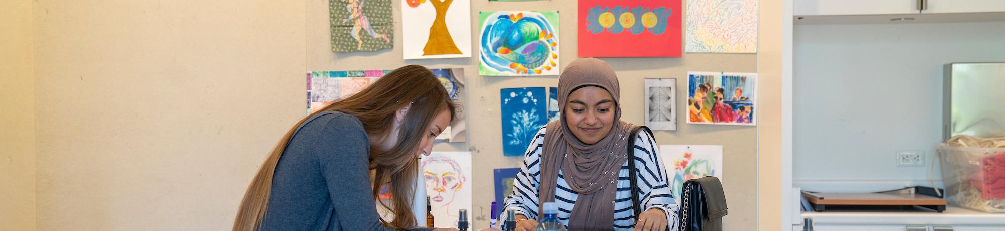 Two students work at a table surrounded by art at UC Davis. 