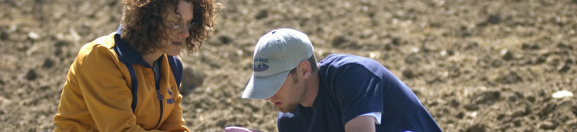 two uc davis students lean over working in dirt field