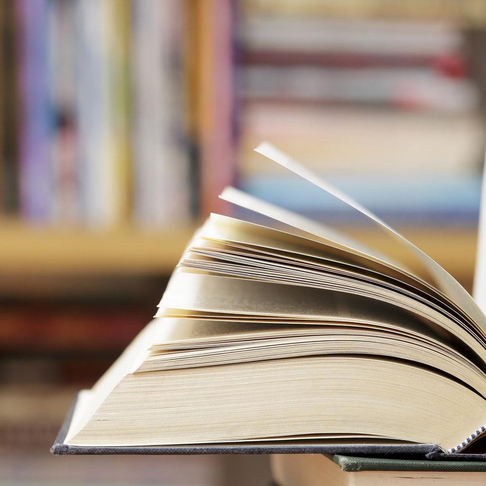 Closeup of a books pages turning with blurred bookshelves in the background