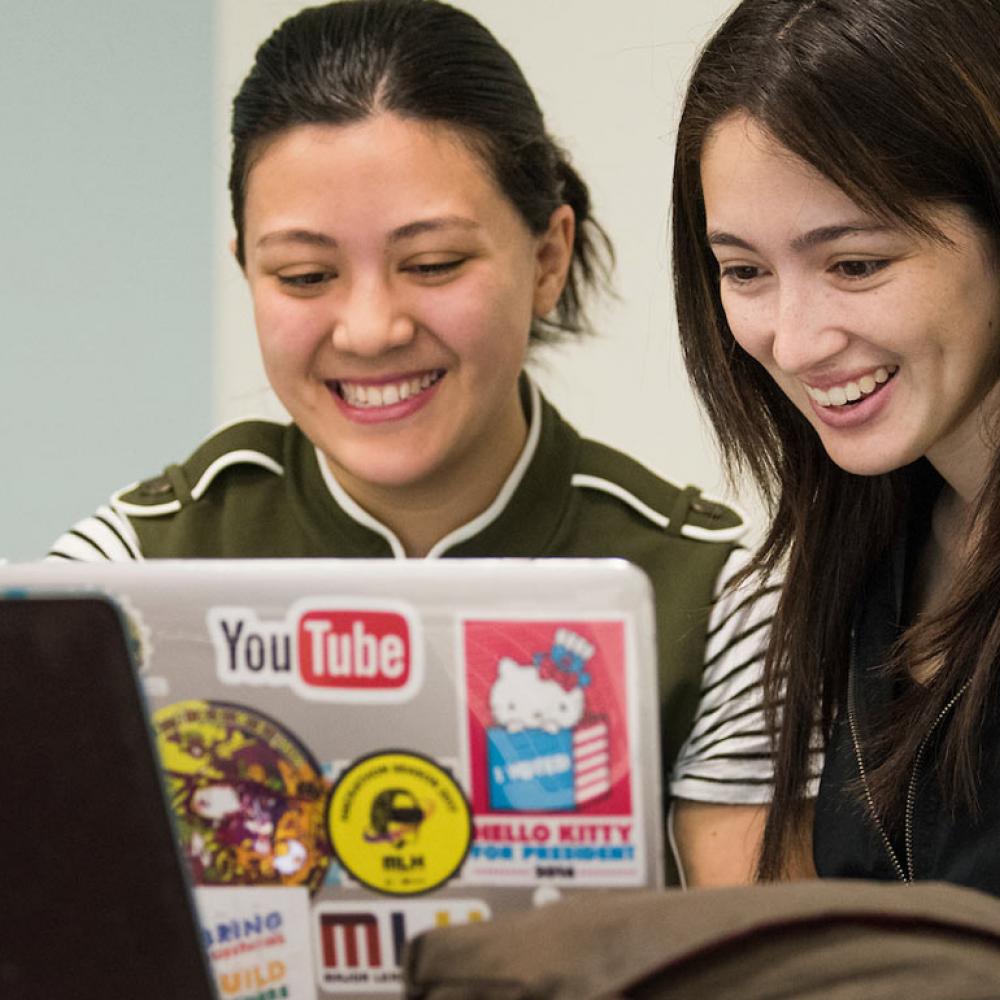 Two female students share a laptop to evaluate their work.