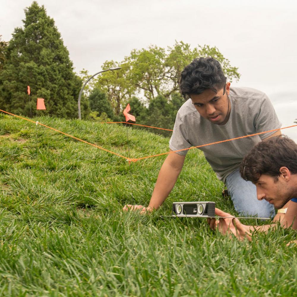 Two male students survey a landscape site with one of the UC Davis eggheads in the background