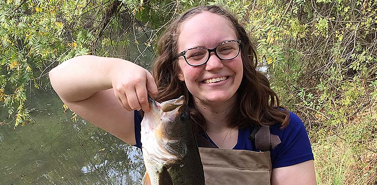 Woman standing in a stream holding a big fish